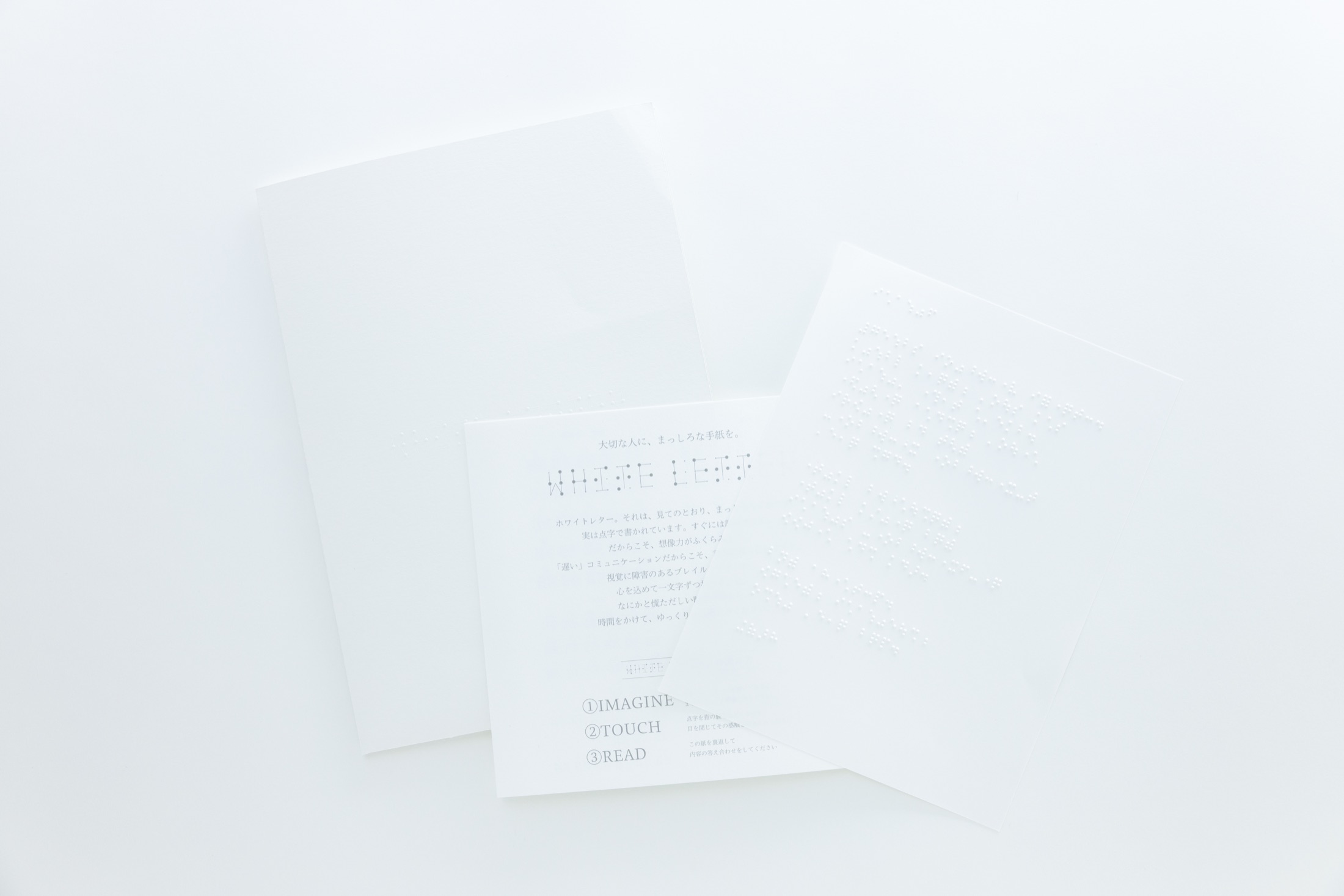 白い台の上に並べられた White Letter 一式。まっしろな封筒と、点字が浮き出た便箋、読み解き方を記したガイドカード
