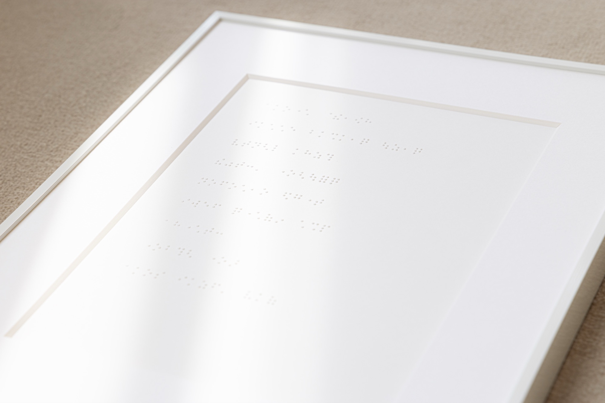 白い額に納められたホワイトレター。斜めからの光で、点字の凹凸が白い紙面に浮かび上がっている